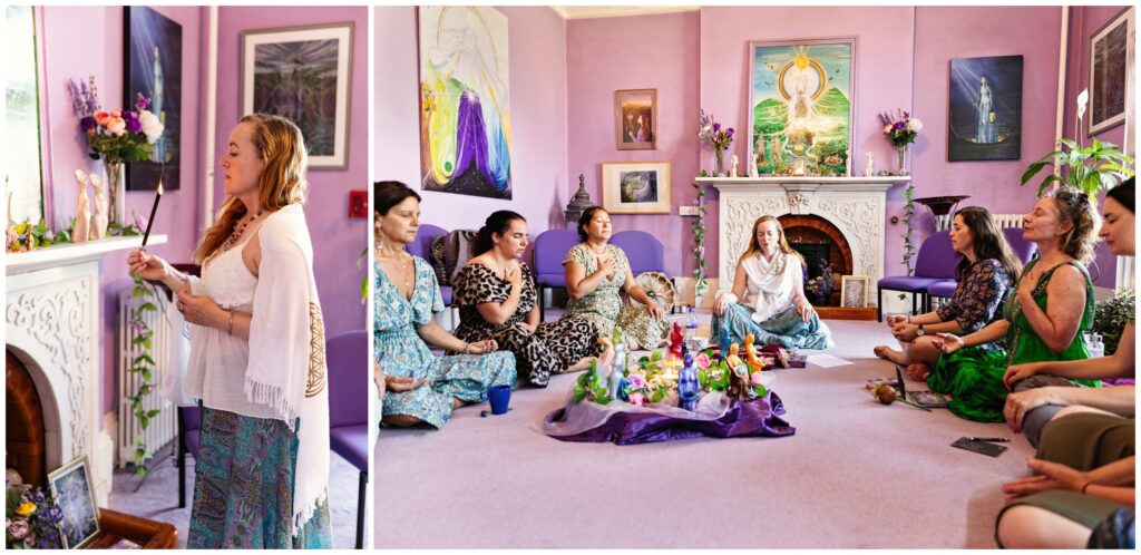 Women gathered in a sacred ceremony circle in the pink and purple room at Goddess House in Glastonbury, with a Priestess lighting an incense stick